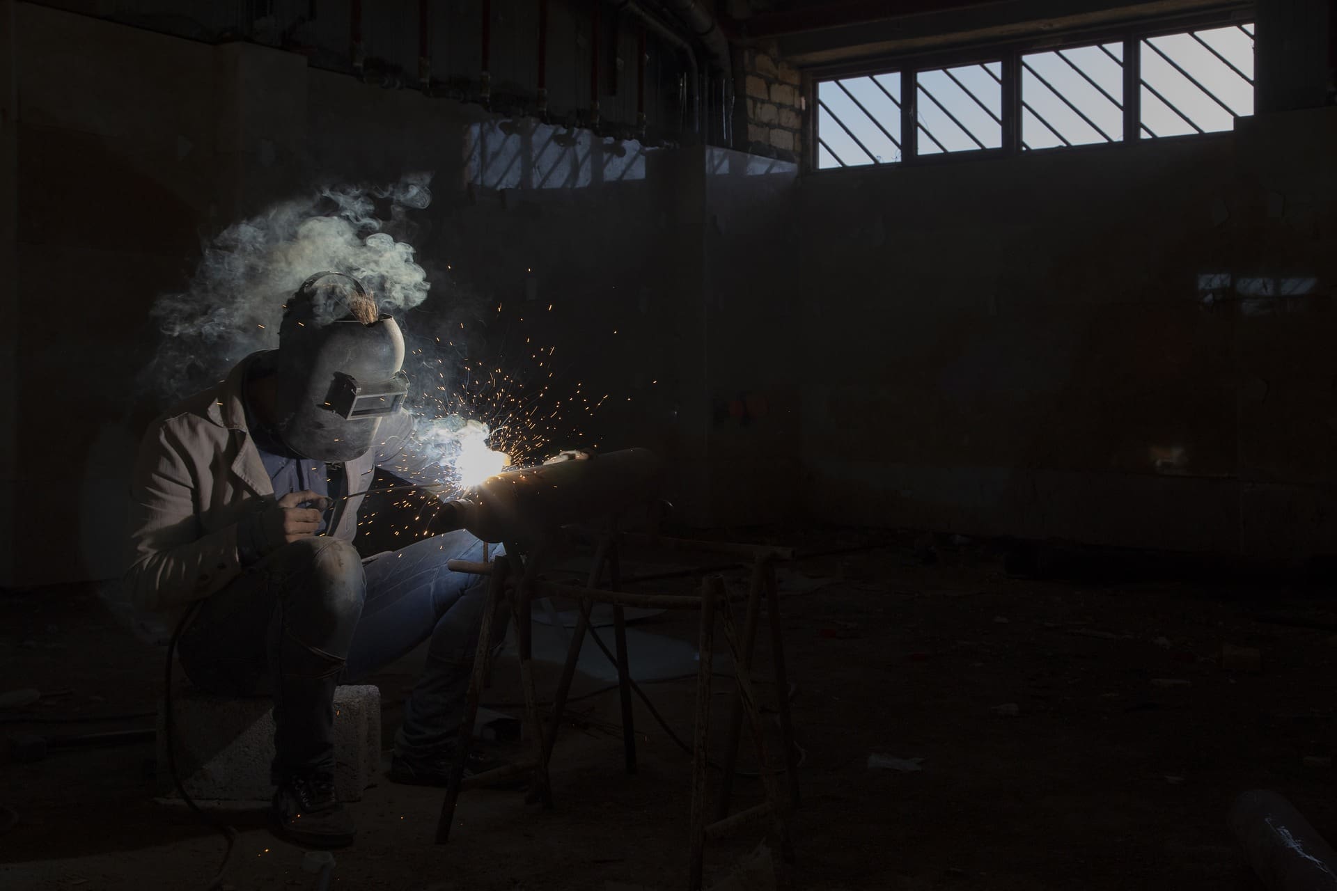 A person welding in an industrial setting with smoke coming out of the windows.